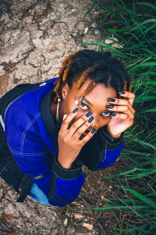 a woman with blue and black nails sitting in the grass