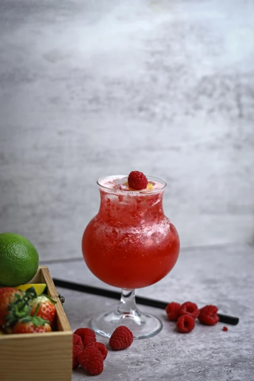 a raspberry margarita sits next to a box of strawberries and limes