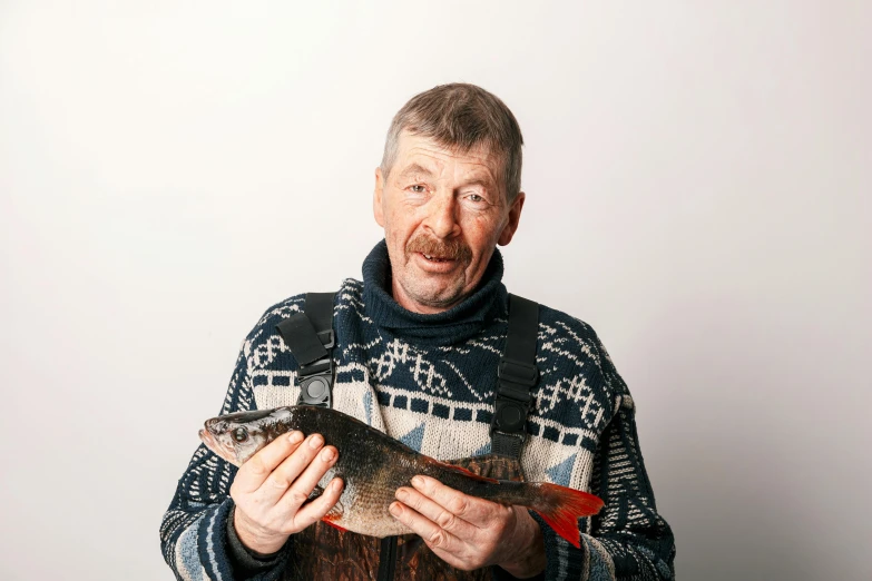 the man is holding a fish while wearing a sweater