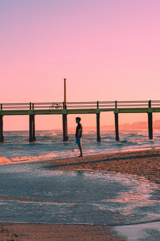 a man standing in the water by a dock at sunset