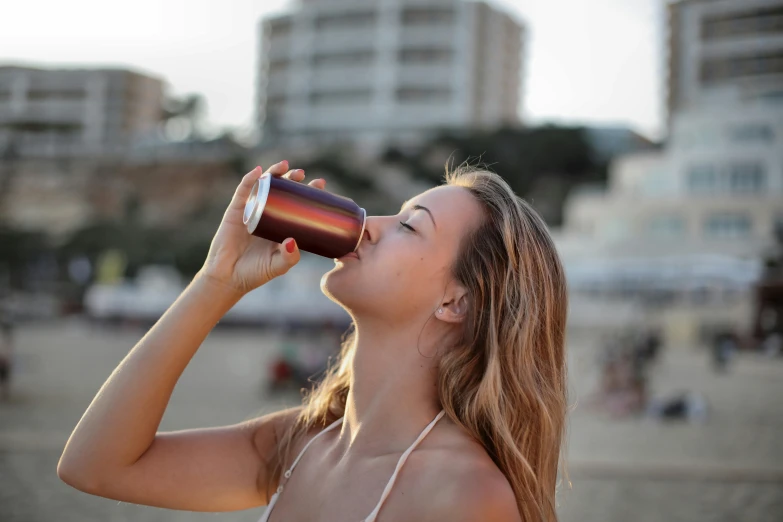 a woman drinking from a can while standing on the beach