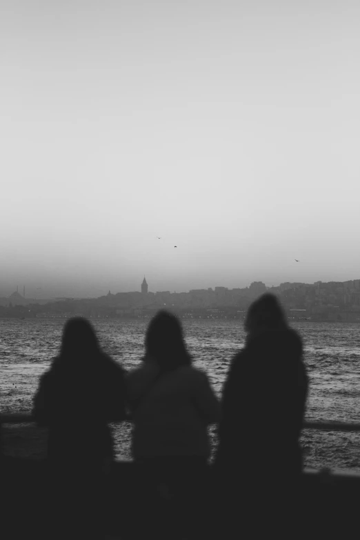 four people sitting next to each other on a shore near the water