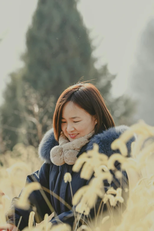 an asian woman stands in a field wearing a blue coat