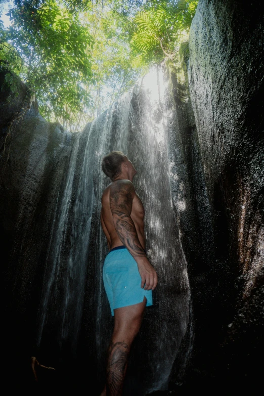 a man in a blue trunks is walking under a waterfall