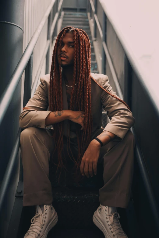 a man with long blonde hair sitting in front of an escalator