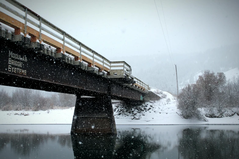 a train crossing a bridge over a river in a snowstorm