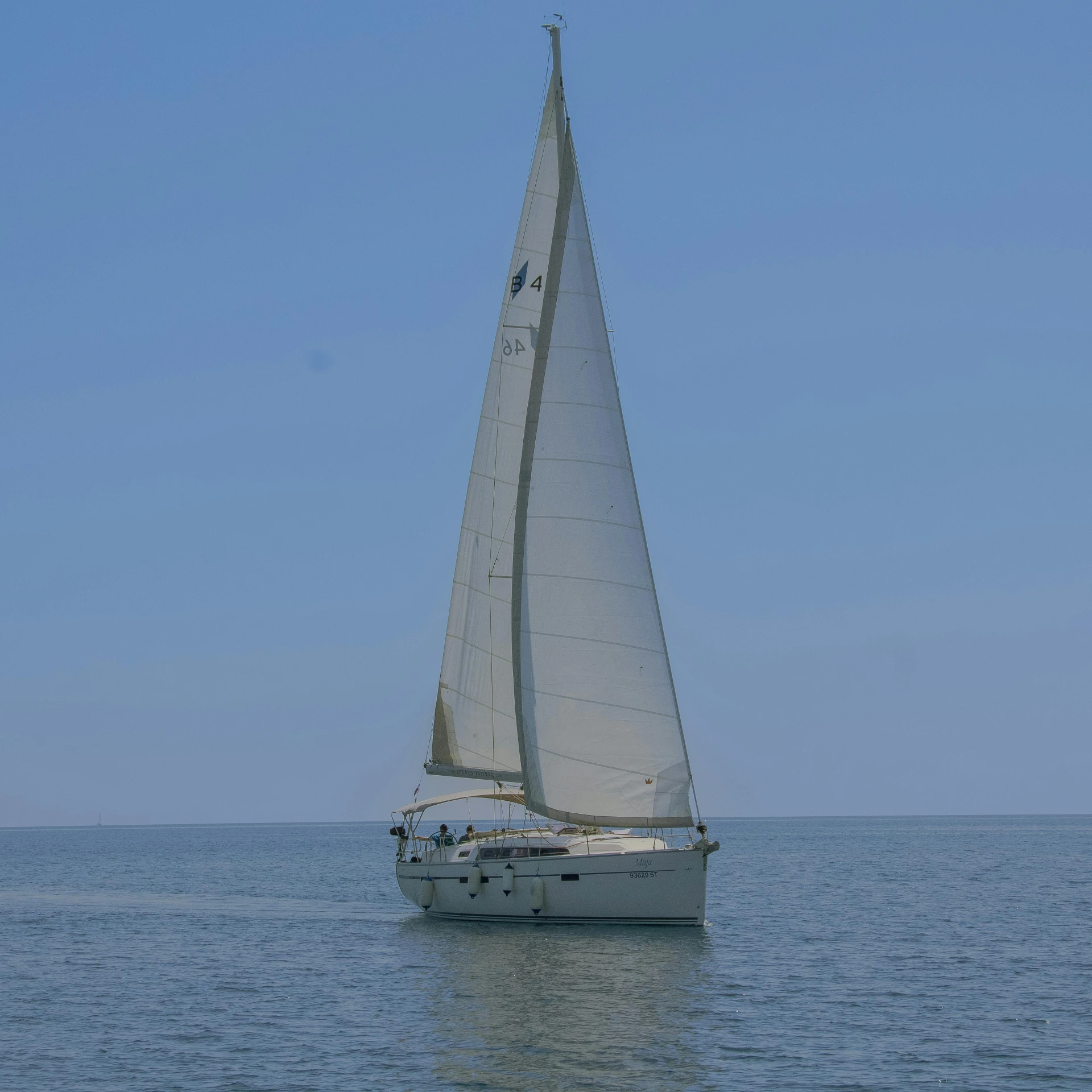 a sail boat with white sails sails across the water