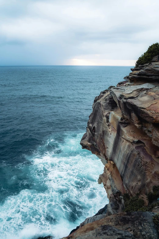 a rocky cliff next to the ocean on a stormy day