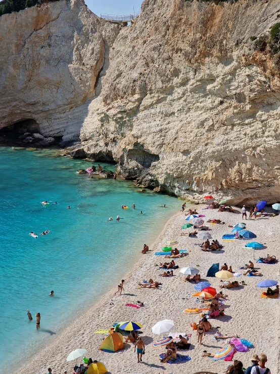 people at beach near cliffs and water with blue sky