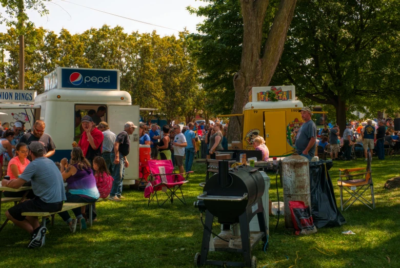 many people are gathered in the shade outside at an outdoor party