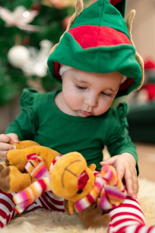 a young baby girl wearing elfs hat holding onto a teddy bear