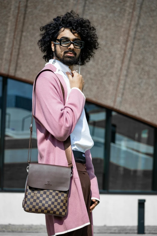 a bearded man with a pink coat and tie looks up while holding a brown louis vuittot bag