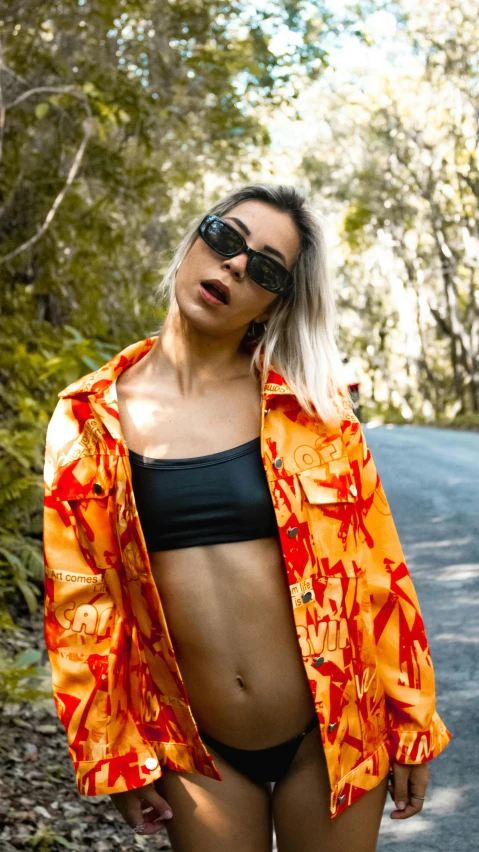 a pregnant woman poses in a bikini by a wooded road