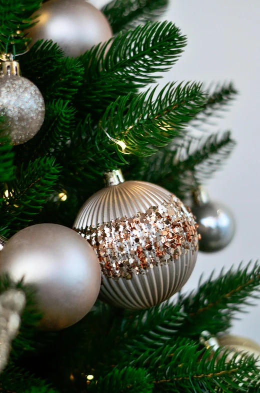 christmas ornaments hang from a nch of a green tree