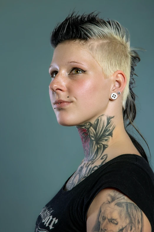 a tattooed woman with tattoos and piercings stands against a grey background