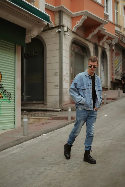 a man in sunglasses and denim jacket standing on the street