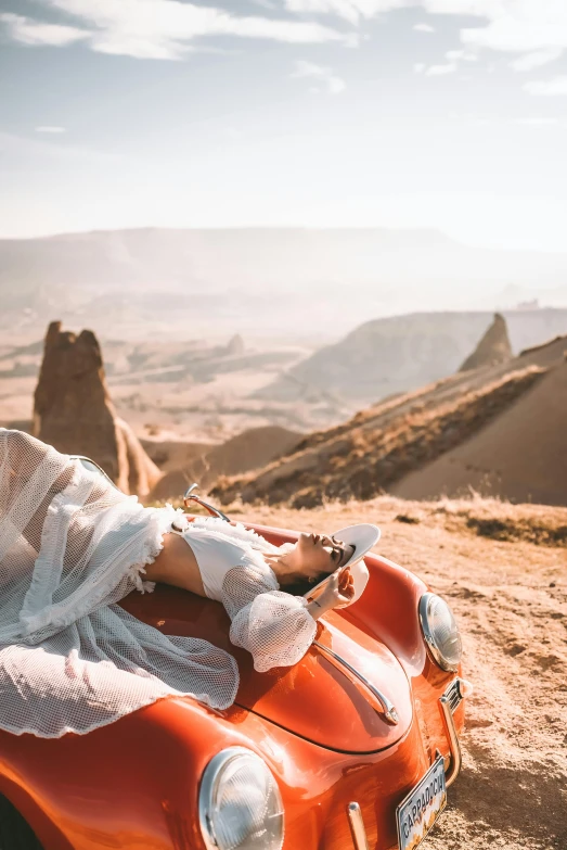 a woman sitting in an orange car on a desert