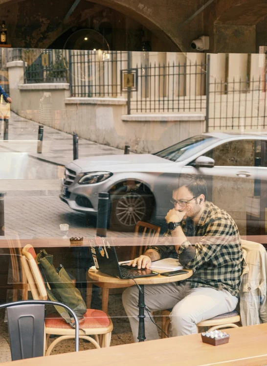 a man sitting at a table in front of a window working on a laptop