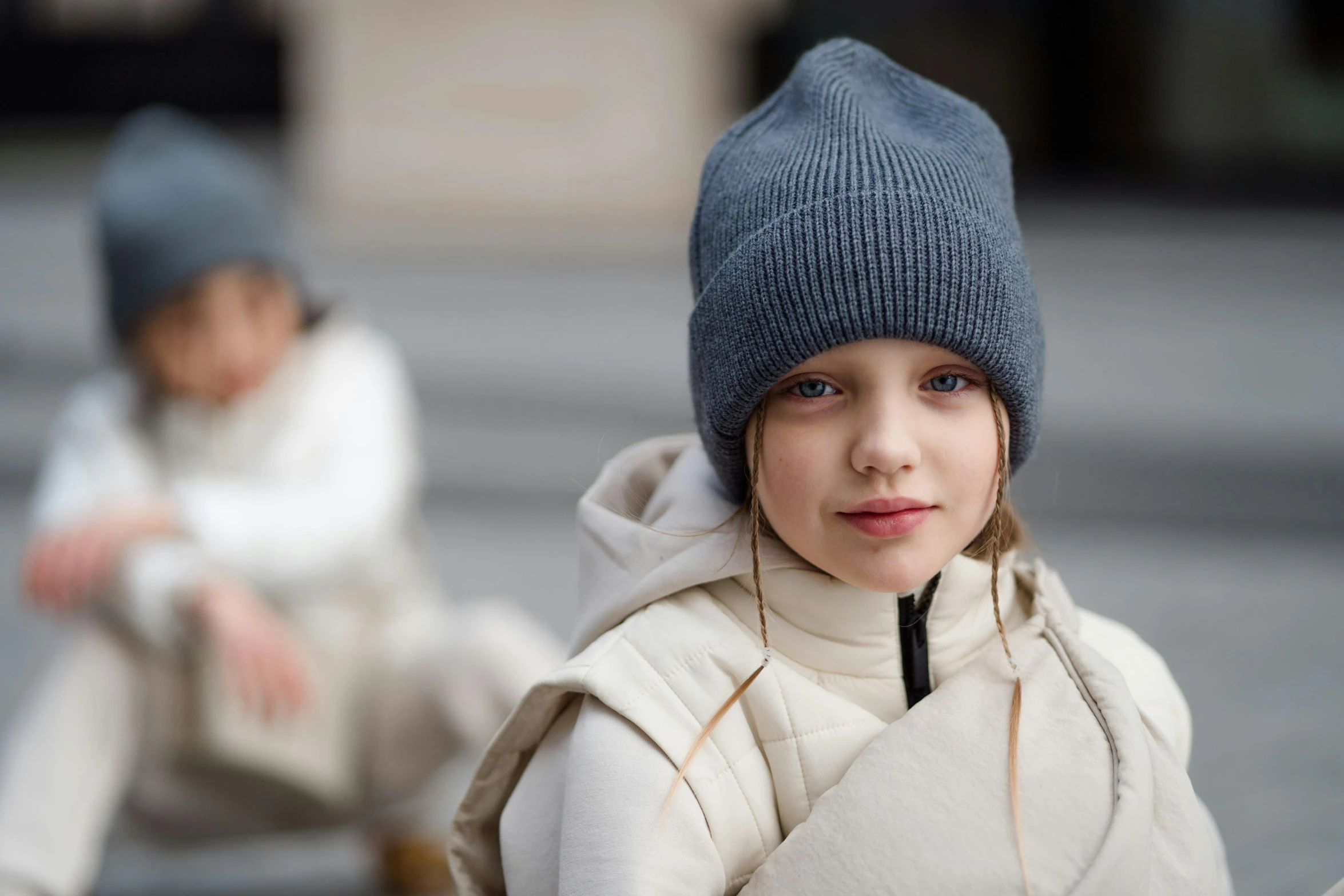 little girl is sitting down wearing a hat and jacket
