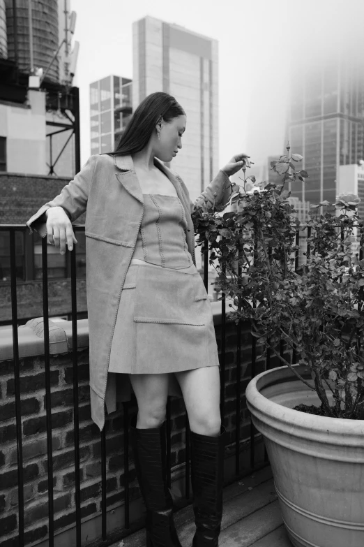 a woman dressed in high boots is standing next to a potted plant