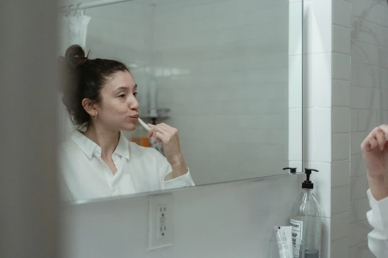 woman brushing her teeth in a mirror next to a sink