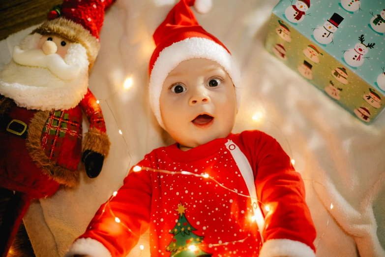 a baby in a red christmas outfit with an illuminated teddy bear