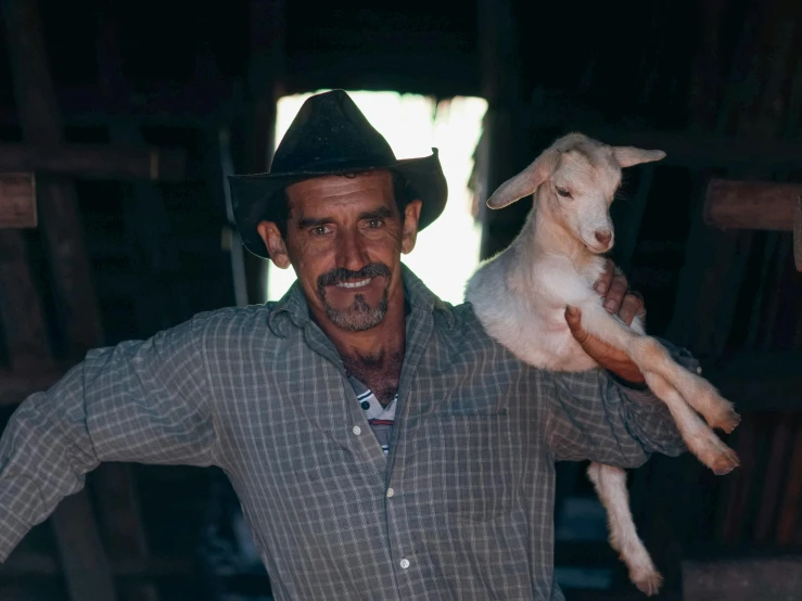 the man has a goat in his arm and he is holding a sheep