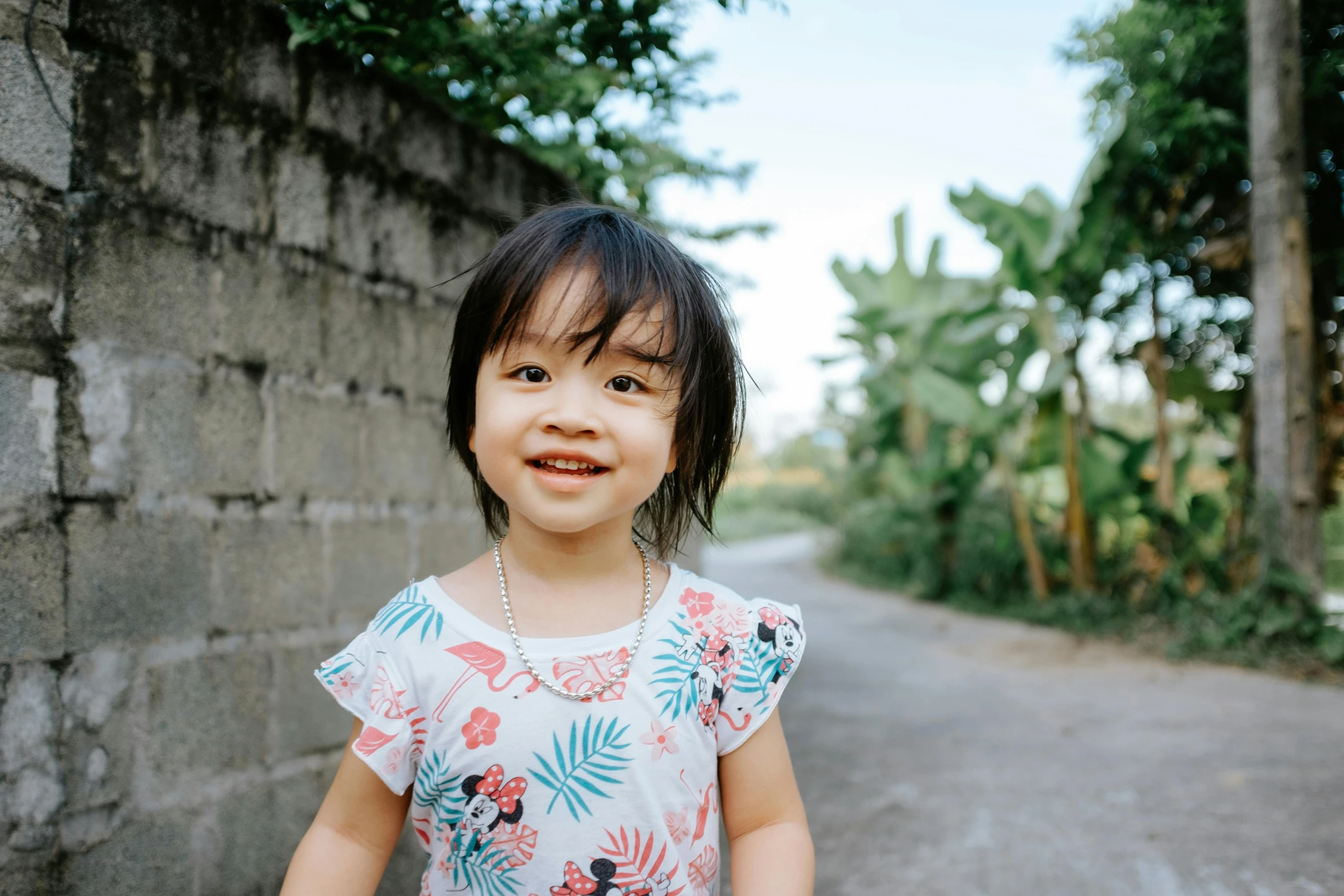 young child smiling in the road near the woods