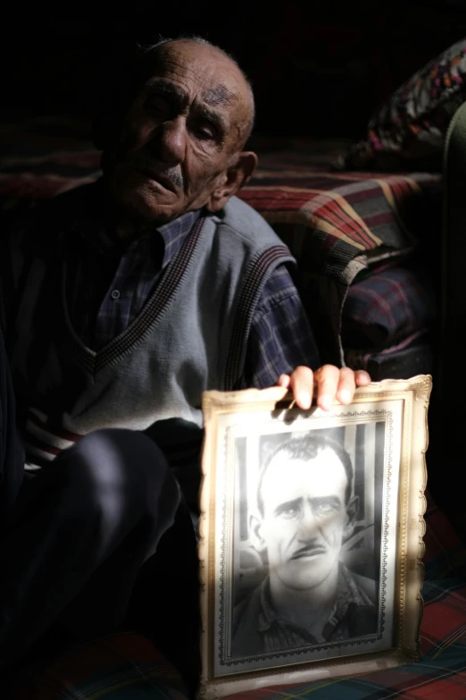 a man sitting down holding a po next to an empty framed pograph