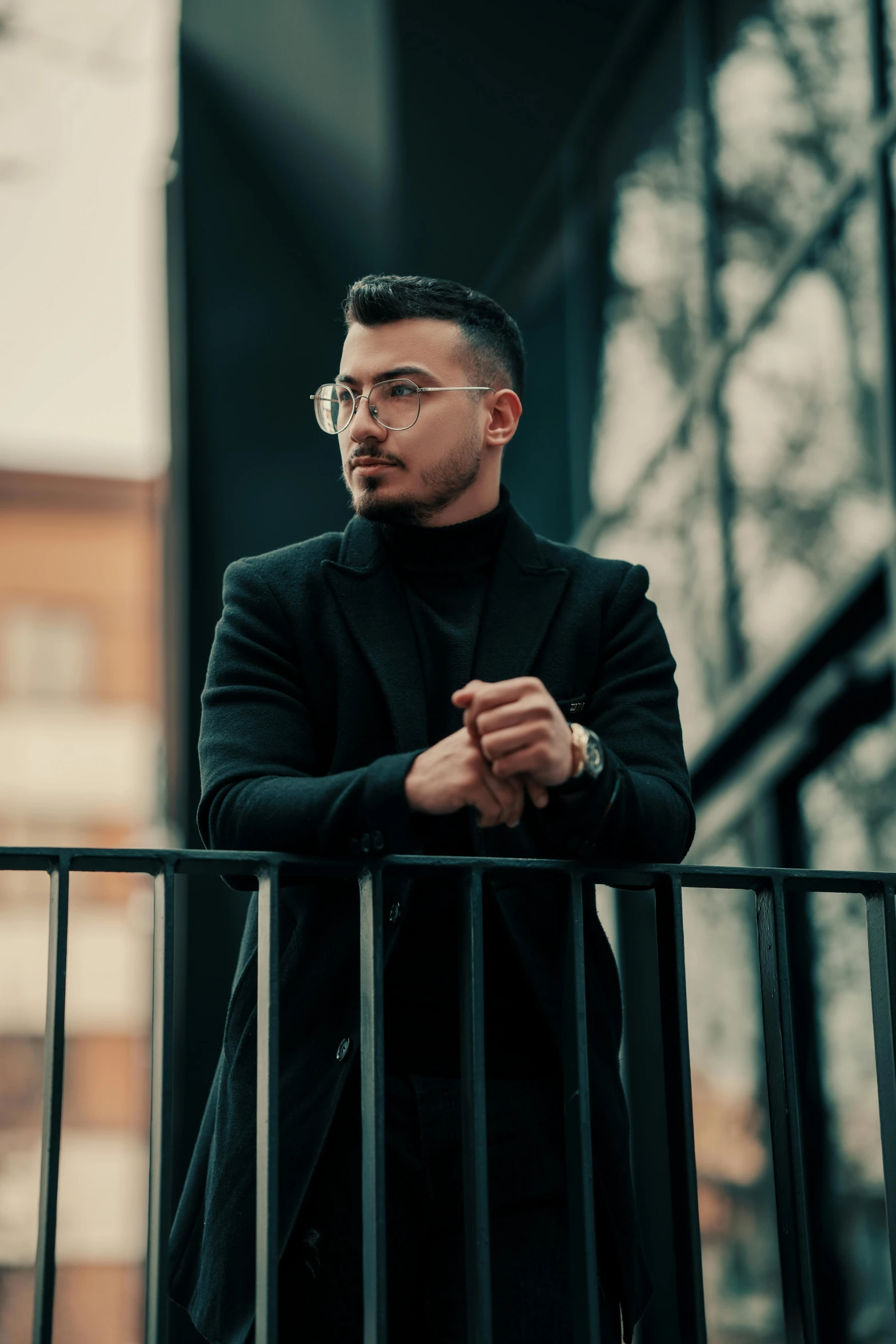 man in glasses stands on balcony railing looking around