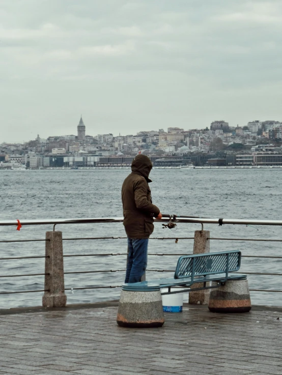 a man fishing in a body of water next to a blue bench