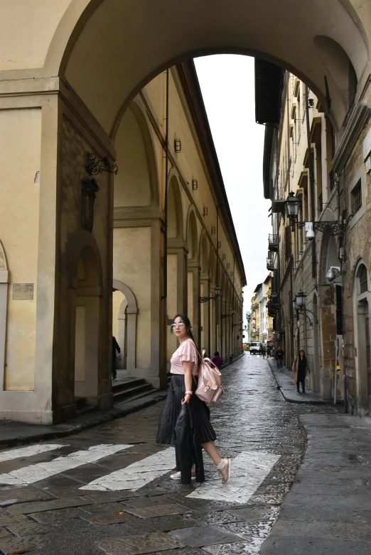 a woman in pink shirt carrying bags standing on street next to buildings