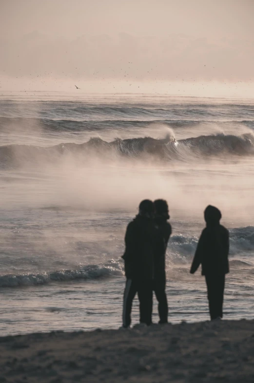 two people standing on the shore of a beach as the waves crash