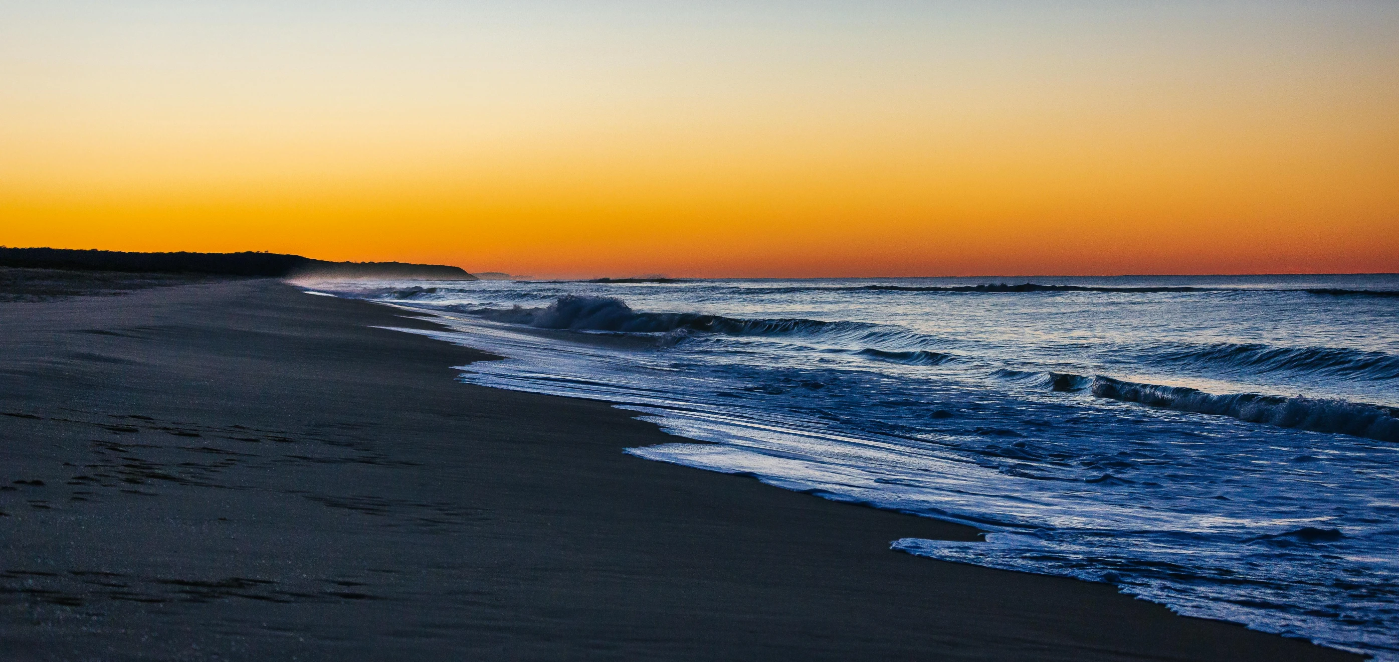 a beautiful sunset seen on the ocean with waves crashing onto the beach