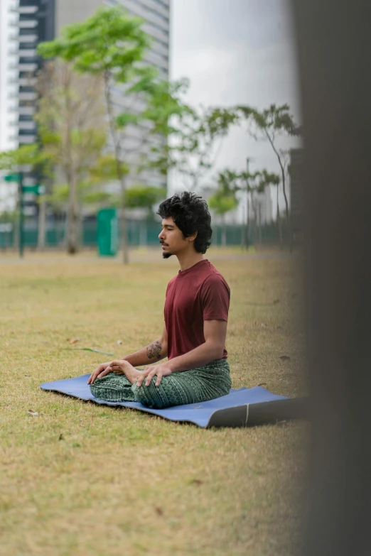 a man sits on a mat in a park, in a yoga pose