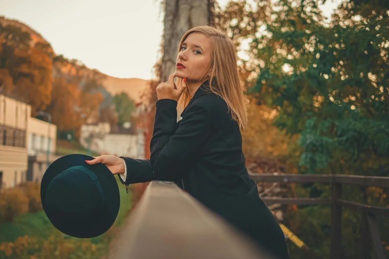 a woman with a hat stands by the edge of a bridge