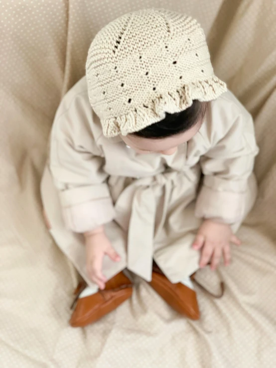 a baby dressed in white sits on the ground and looks up with one foot on the ground