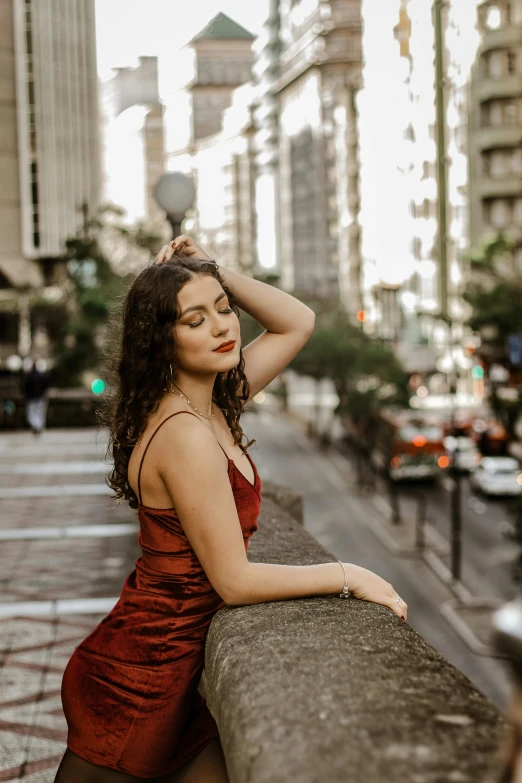 a woman poses by a city street leaning on a railing