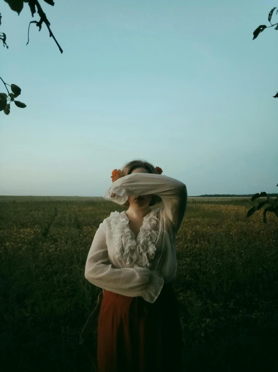 a woman wearing a hat and dress stands in a field