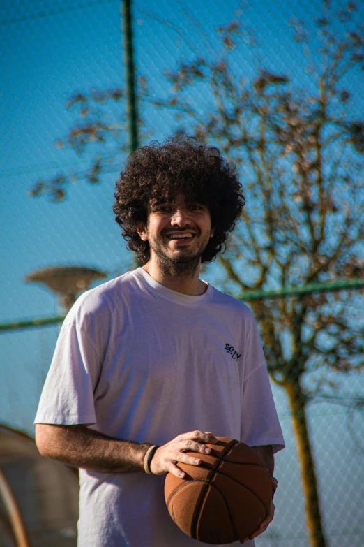 a smiling man holding a basketball by a fence