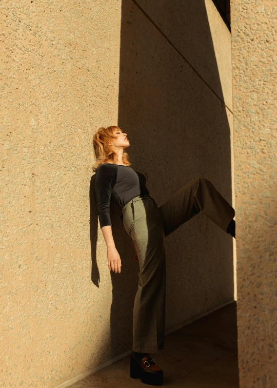 a woman leans against the wall while she is dressed in gray