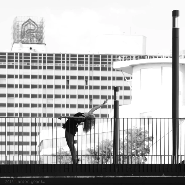 a person leaning against a fence with an ocean and office building in the background