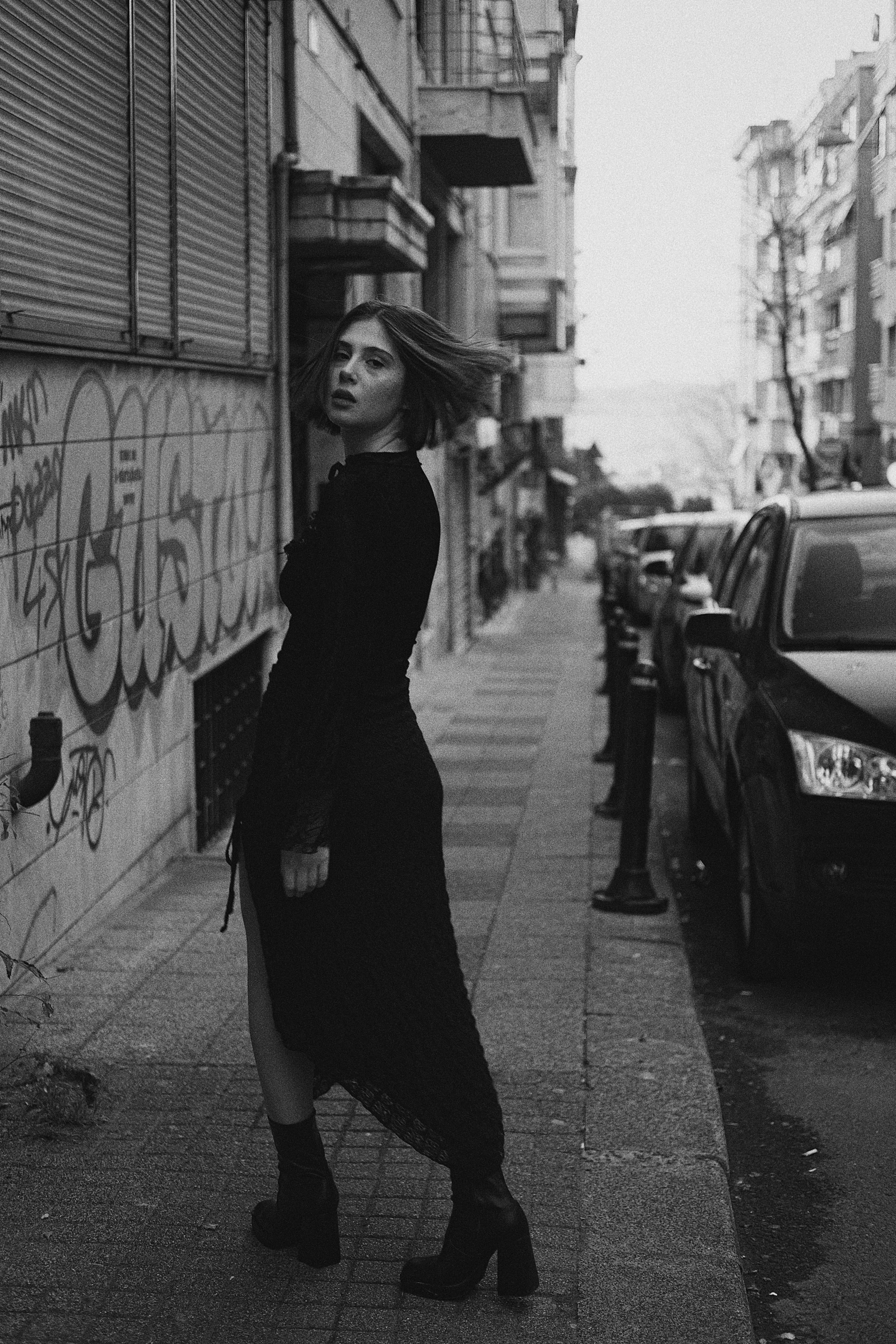 a woman is standing on the sidewalk next to a wall covered with graffiti