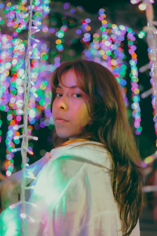 a girl looking up at a pole with colorful lights in the background