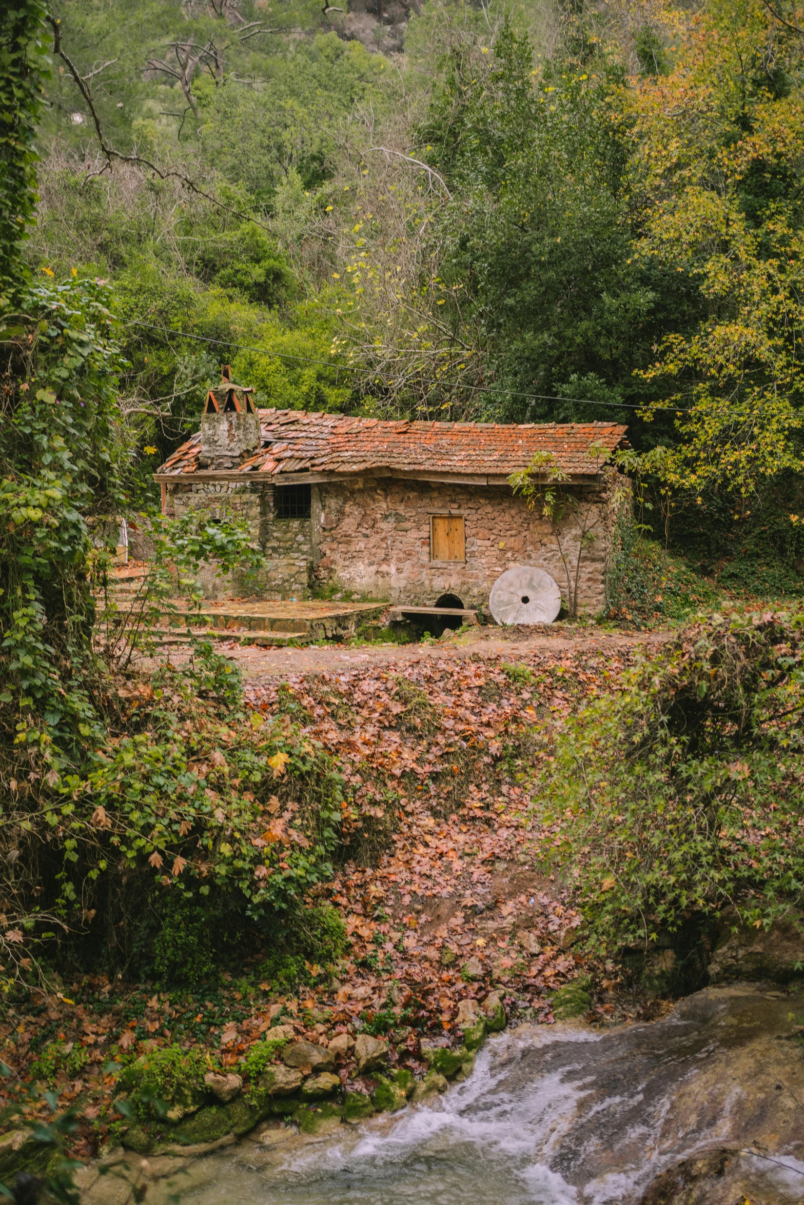 small stone building surrounded by wooded greenery near a river