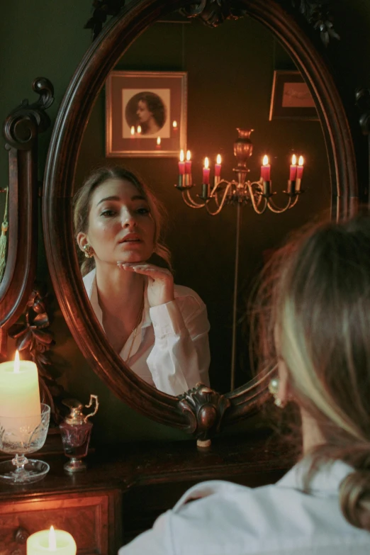 a woman looking in the mirror with a candle near her