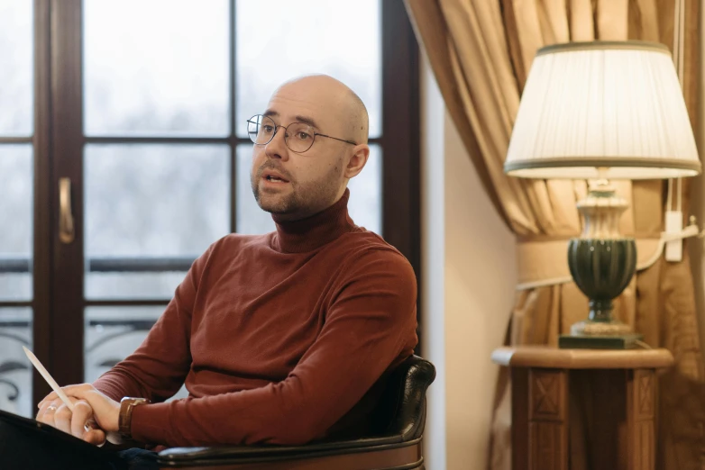 a bald man in red shirt sitting in chair with a lamp on either side