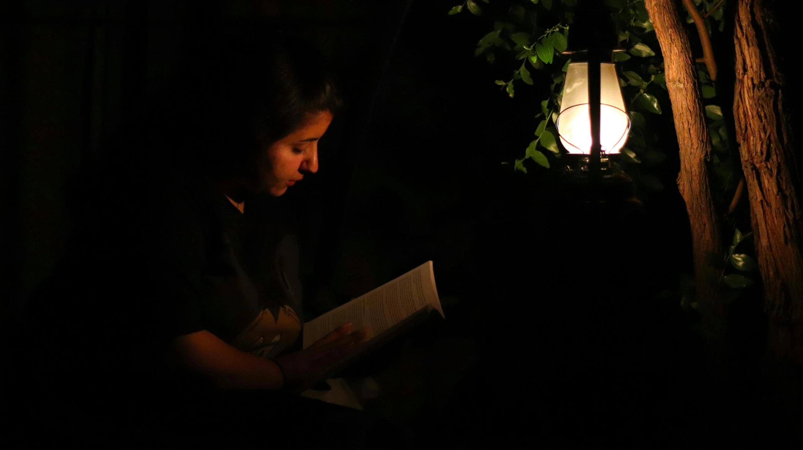 a woman sitting by the table in a dark room and reading