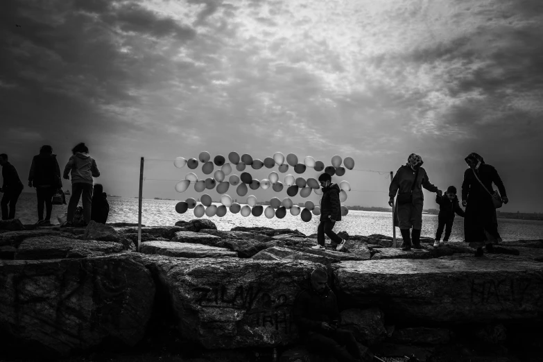 several people are gathered on the edge of a cliff with balloons floating