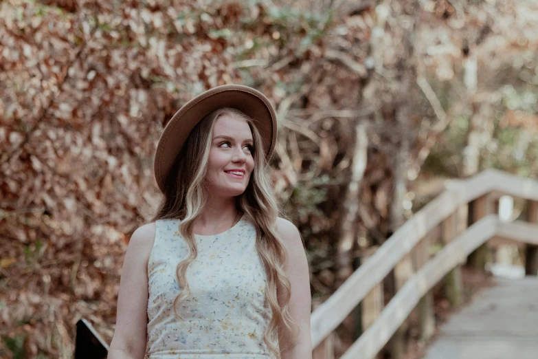 a woman in a hat smiling and standing on a bridge